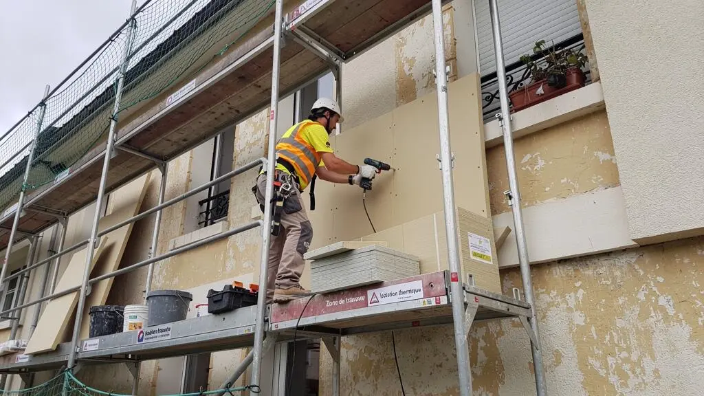 Ouvrier installant des panneaux d'isolation thermique sur la façade d'un immeuble résidentiel depuis un échafaudage